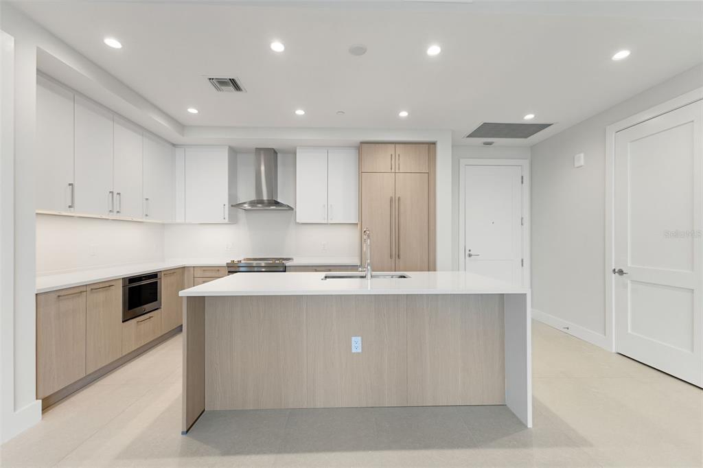 A modern kitchen features white upper cabinets, light wood lower cabinets, and a central island — 275 1ST AVENUE S UNIT 2308, ST PETERSBURG, FL