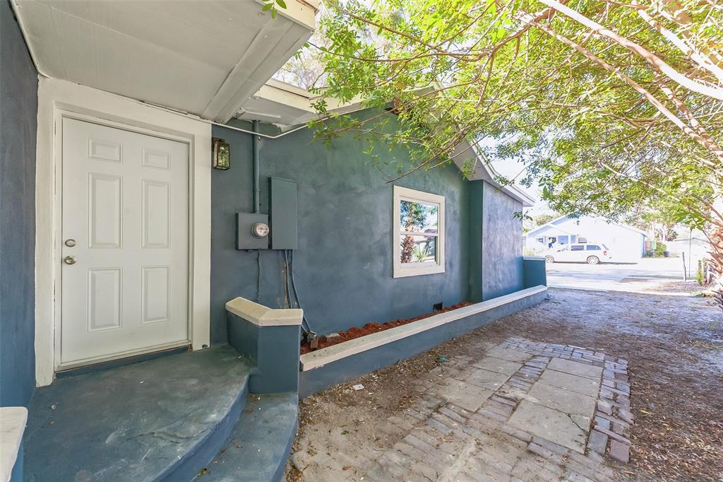 A blue exterior wall with a white door, a small window, and a brick patio — 3458 QUEENSBORO AVENUE S, ST PETERSBURG, FL