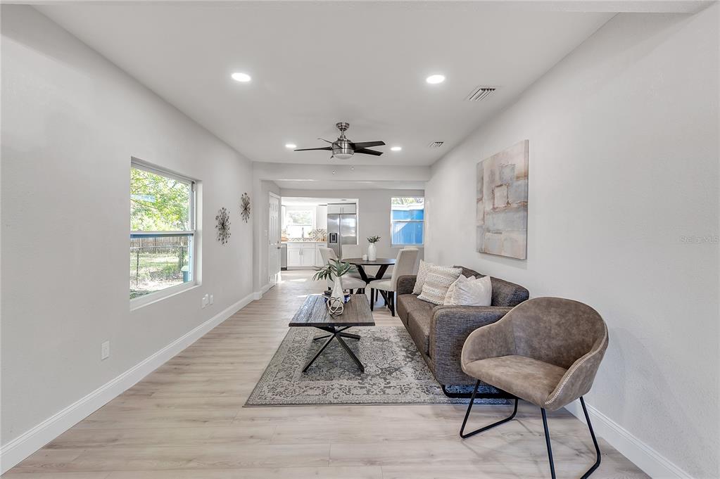 An open-concept living and dining area features light wood flooring, a ceiling fan, and furniture — 3458 QUEENSBORO AVENUE S, ST PETERSBURG, FL