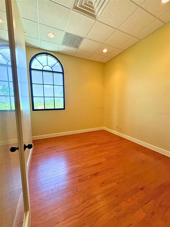 An empty room features light wood flooring, a large arched window, and a drop ceiling — 2100 SE HILLMOOR DRIVE UNIT 204A, PORT ST LUCIE, FL