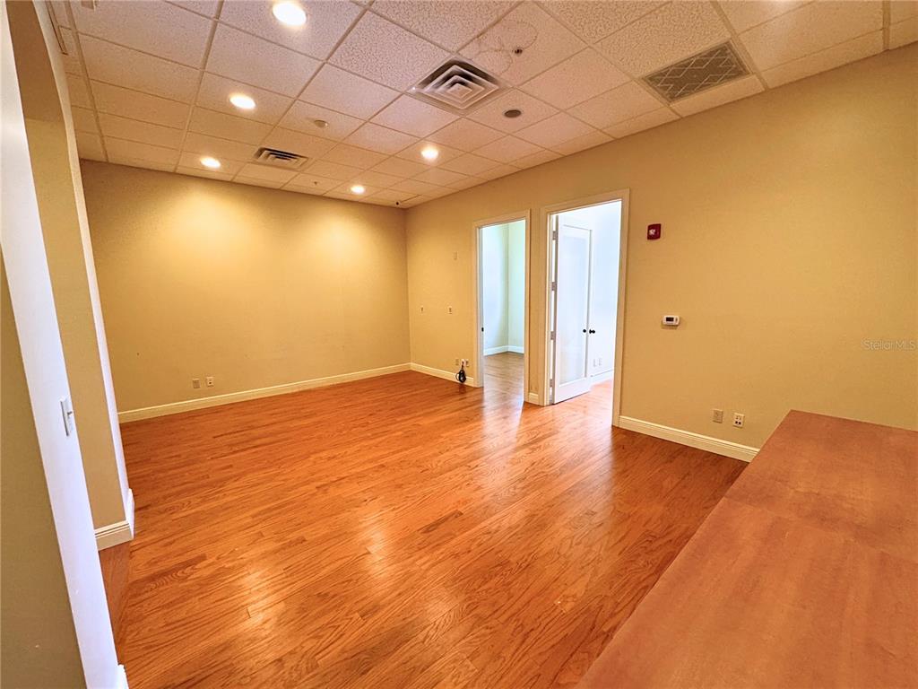 An empty office room with wood flooring, beige walls, and a drop ceiling — 2100 SE HILLMOOR DRIVE UNIT 204A, PORT ST LUCIE, FL