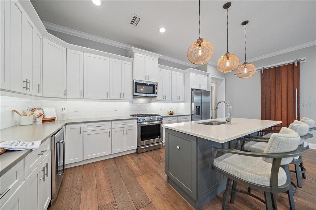 A kitchen features white cabinets, a gray island with seating, and wood flooring — 2207 WISTERIA STREET, SARASOTA, FL