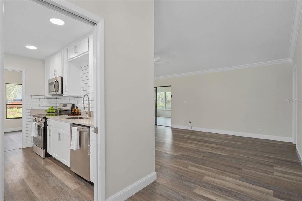 A kitchen with white cabinets and stainless steel appliances opens into a living area — 1033 OLD SOUTH LANE, APOPKA, FL