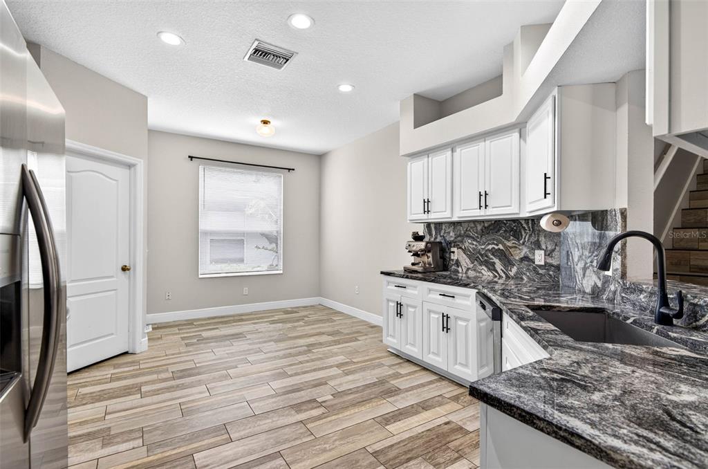 A kitchen with white cabinets, dark granite countertops, and wood-look tile flooring — 10024 COLDWATER LOOP, LAND O LAKES, FL