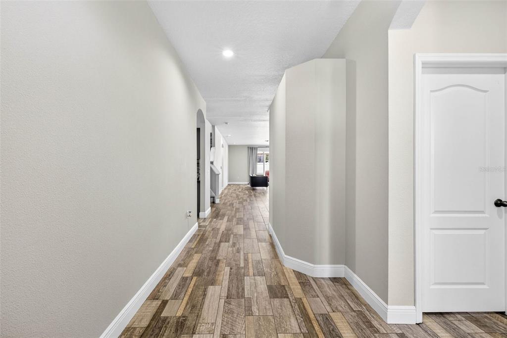 A hallway with wood-look tile flooring leads toward a living area with a white door — 10024 COLDWATER LOOP, LAND O LAKES, FL