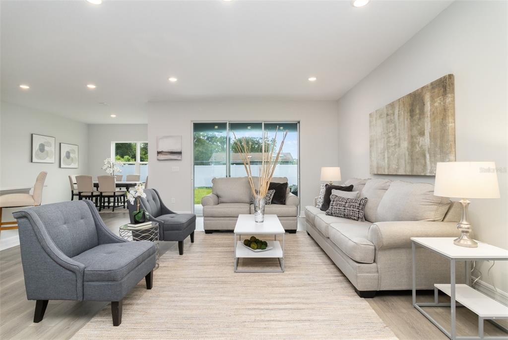 A living room with light gray walls, wood-look flooring, and neutral furniture faces a sliding door — 12 S SCHOOL AVENUE, LECANTO, FL