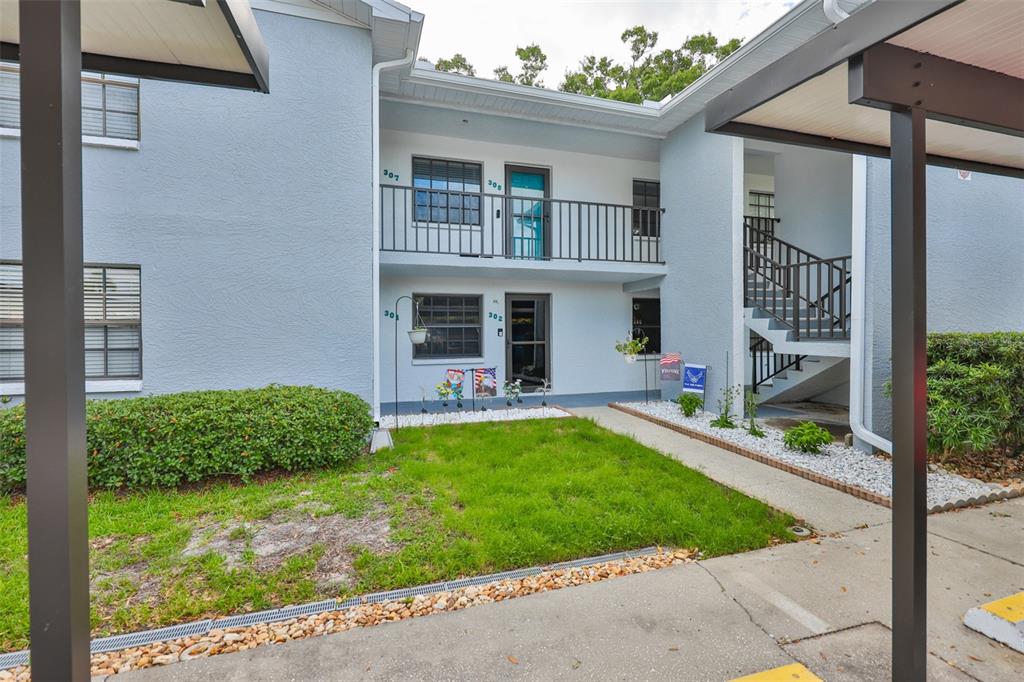 A two-story apartment building exterior features a grassy lawn, a staircase, and covered parking — 11800 PARK BOULEVARD UNIT 308, SEMINOLE, FL