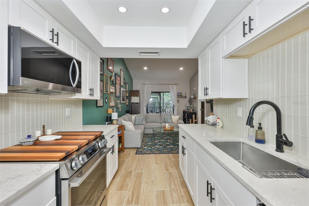 A galley kitchen with white cabinets and quartz countertops opens into a living room area — 11800 PARK BOULEVARD UNIT 308, SEMINOLE, FL