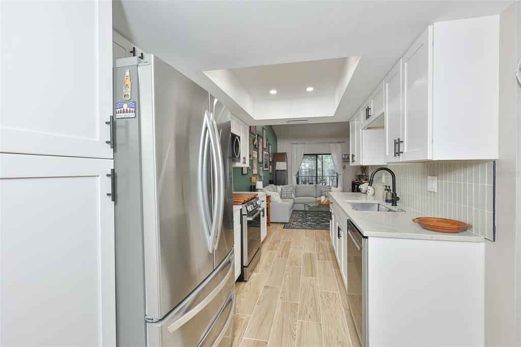 A galley kitchen features white cabinets, stainless steel appliances, and light wood-look tile flooring — 11800 PARK BOULEVARD UNIT 308, SEMINOLE, FL