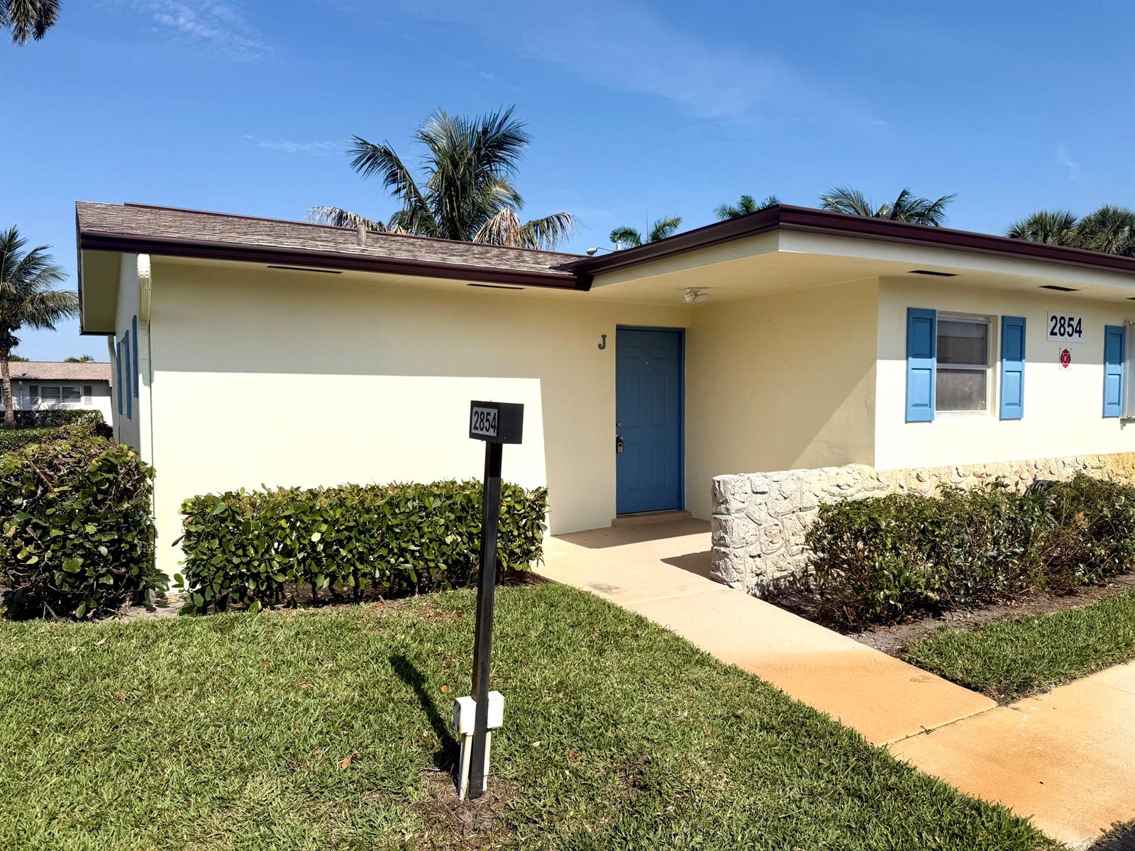 A single-story building with a blue door, blue shutters, and a stone accent wall — 2854 E Crosley Dr Drive E # J, West Palm Beach FL 33415, WEST PALM BEACH, FL