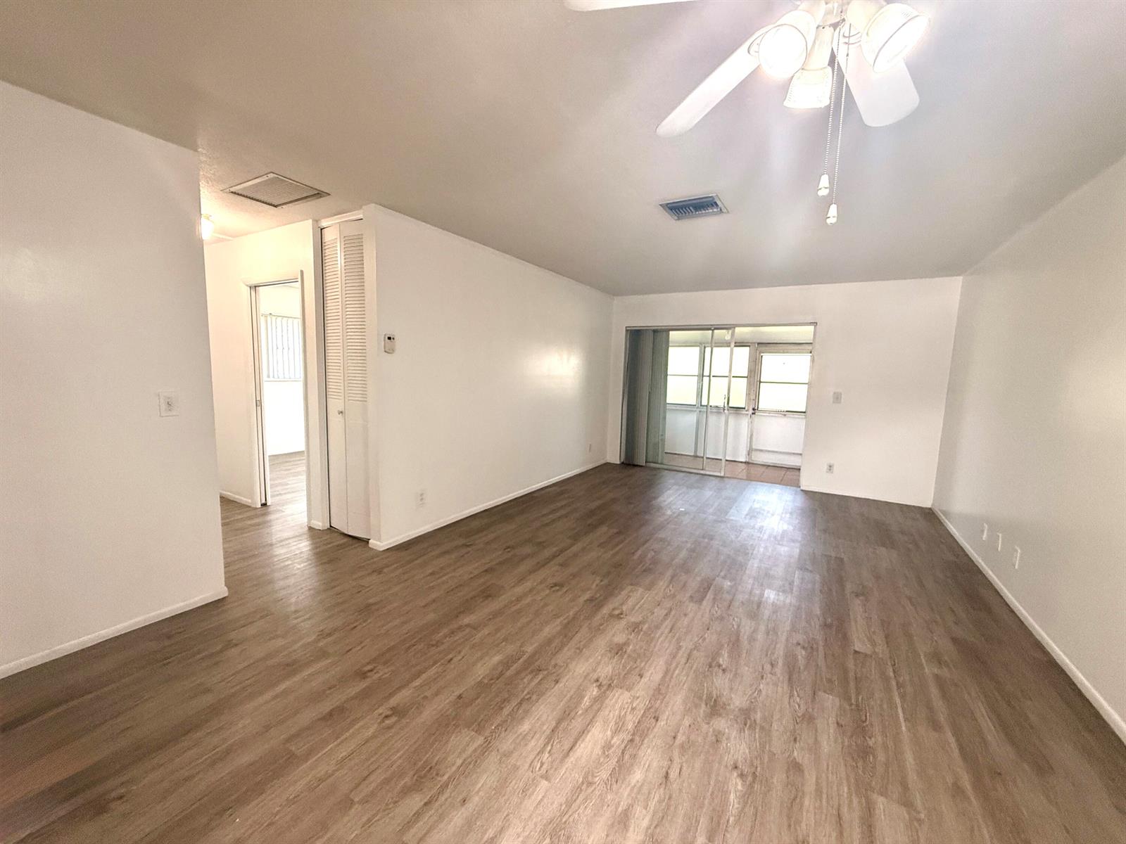 An empty living room features white walls, wood-look flooring, a ceiling fan, and sliding glass doors — 2854 E Crosley Dr Drive E # J, West Palm Beach FL 33415, WEST PALM BEACH, FL