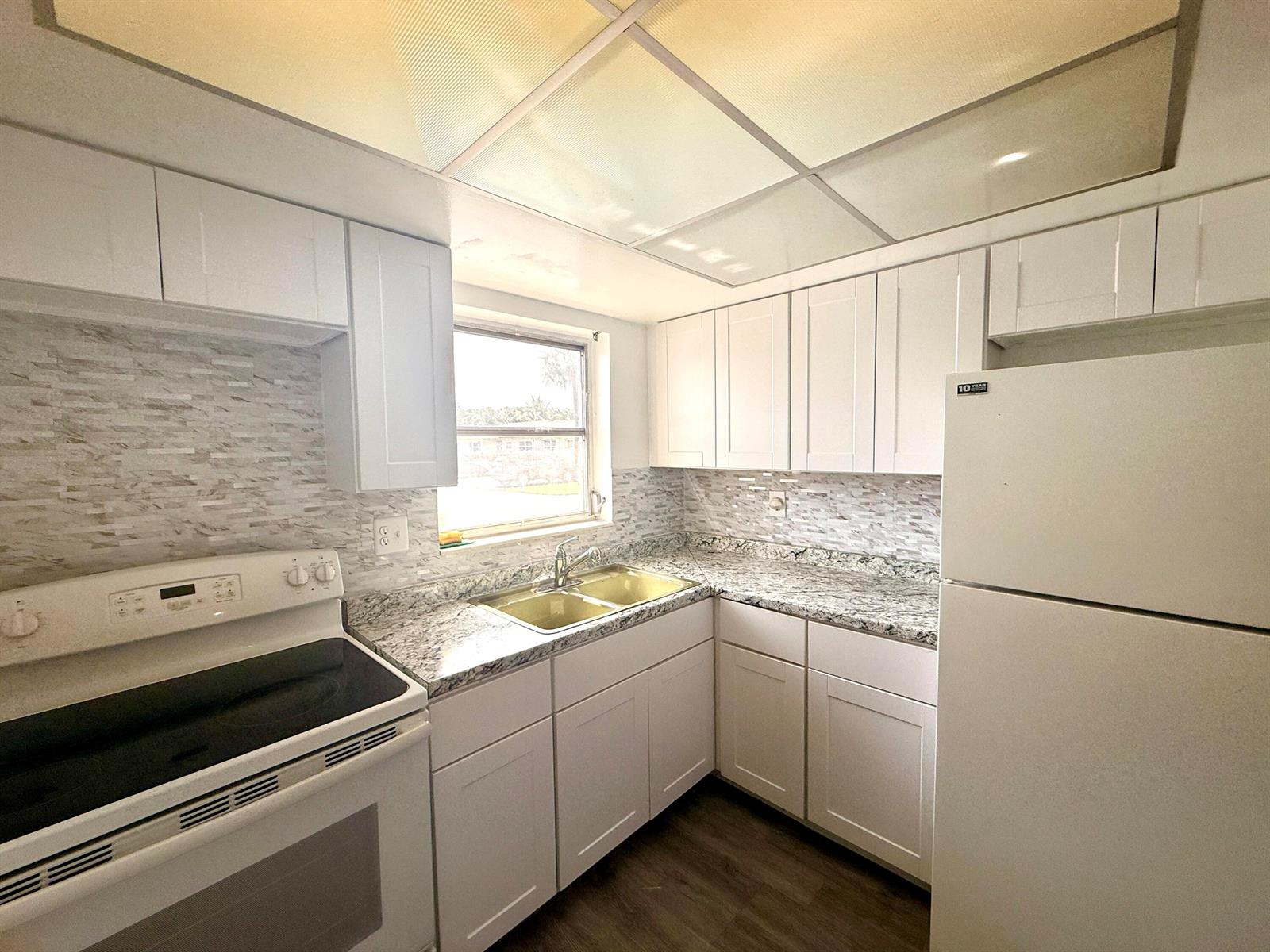 A kitchen features white cabinets, granite countertops, a tiled backsplash, and a white stove — 2854 E Crosley Dr Drive E # J, West Palm Beach FL 33415, WEST PALM BEACH, FL