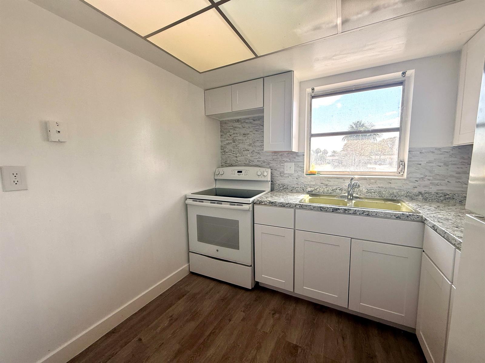 A kitchen features white cabinets, a white electric stove, a window, and granite-look countertops — 2854 E Crosley Dr Drive E # J, West Palm Beach FL 33415, WEST PALM BEACH, FL