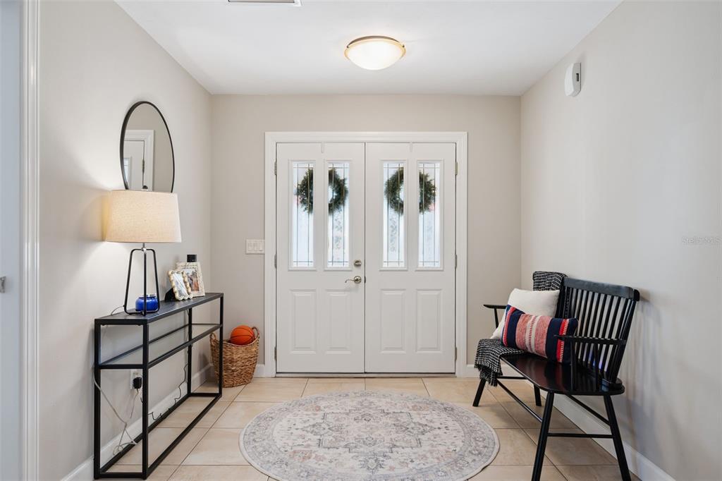 An entryway features a double front door, a console table, a bench, and tile flooring — 102 ASPEN PLACE, LONGWOOD, FL