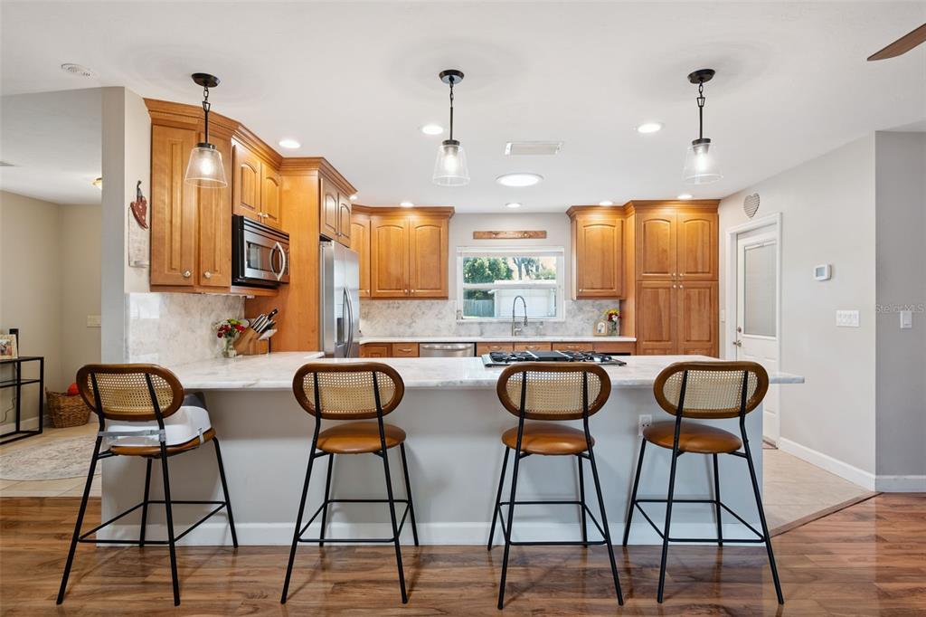 A kitchen features wood cabinets, a marble-topped island with four bar stools, and stainless appliances — 102 ASPEN PLACE, LONGWOOD, FL