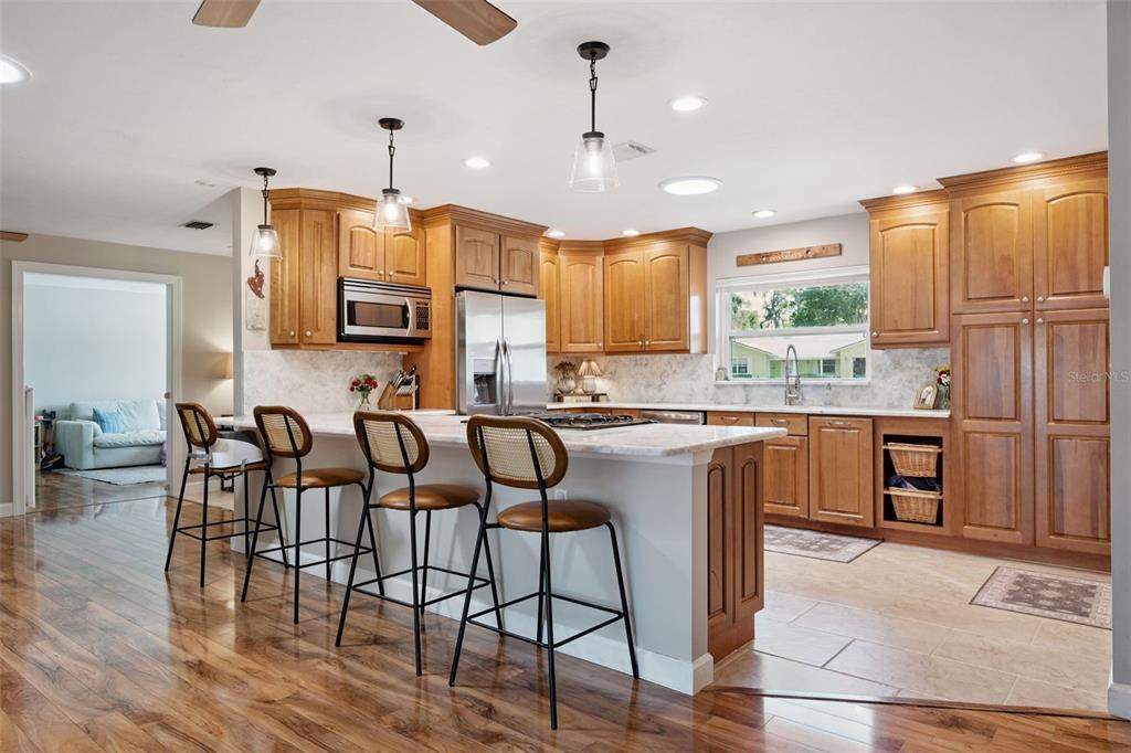 A kitchen features wood cabinets, a marble-topped island with four stools, and hardwood flooring — 102 ASPEN PLACE, LONGWOOD, FL