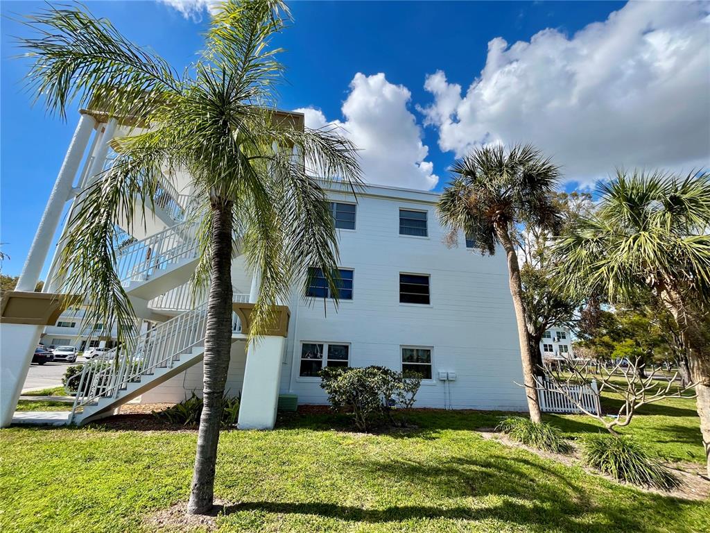 A three-story white apartment building features an exterior staircase and palm trees in the yard — 2430 BRAZILIA DRIVE UNIT 44, CLEARWATER, FL