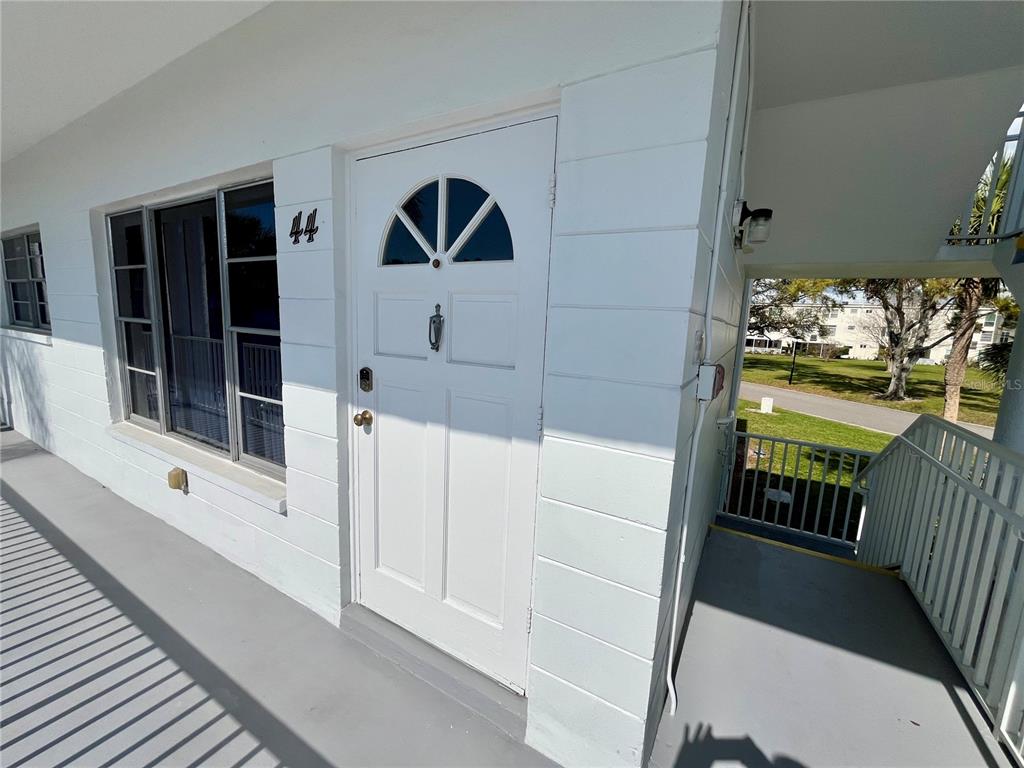 A white exterior door with the number 44 sits on a balcony next to a window — 2430 BRAZILIA DRIVE UNIT 44, CLEARWATER, FL