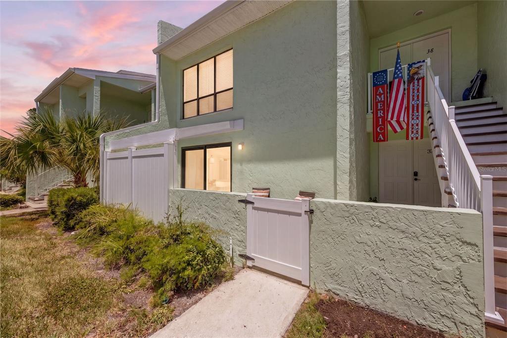 A light green two-story townhouse exterior features a white gate, stairs, and American flag decor — 1 WINDRUSH BOULEVARD UNIT 37, INDIAN ROCKS BEACH, FL