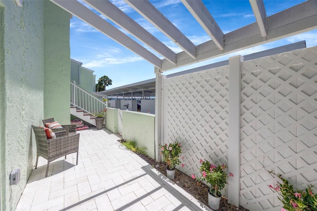 A paved patio features a pergola, a wicker chair, and a white lattice privacy screen — 1 WINDRUSH BOULEVARD UNIT 37, INDIAN ROCKS BEACH, FL