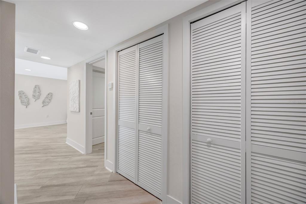 A hallway with light wood-look flooring features two sets of white louvered closet doors — 1 WINDRUSH BOULEVARD UNIT 37, INDIAN ROCKS BEACH, FL