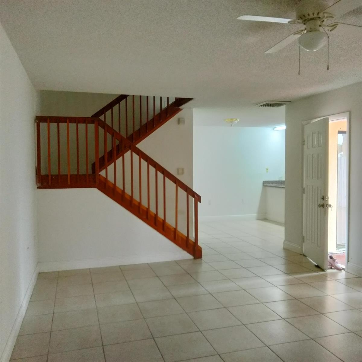 An interior view showing a tiled living area with a wooden staircase and ceiling fan — 729 Mill Valley Place, West Palm Beach FL 33409, WEST PALM BEACH, FL