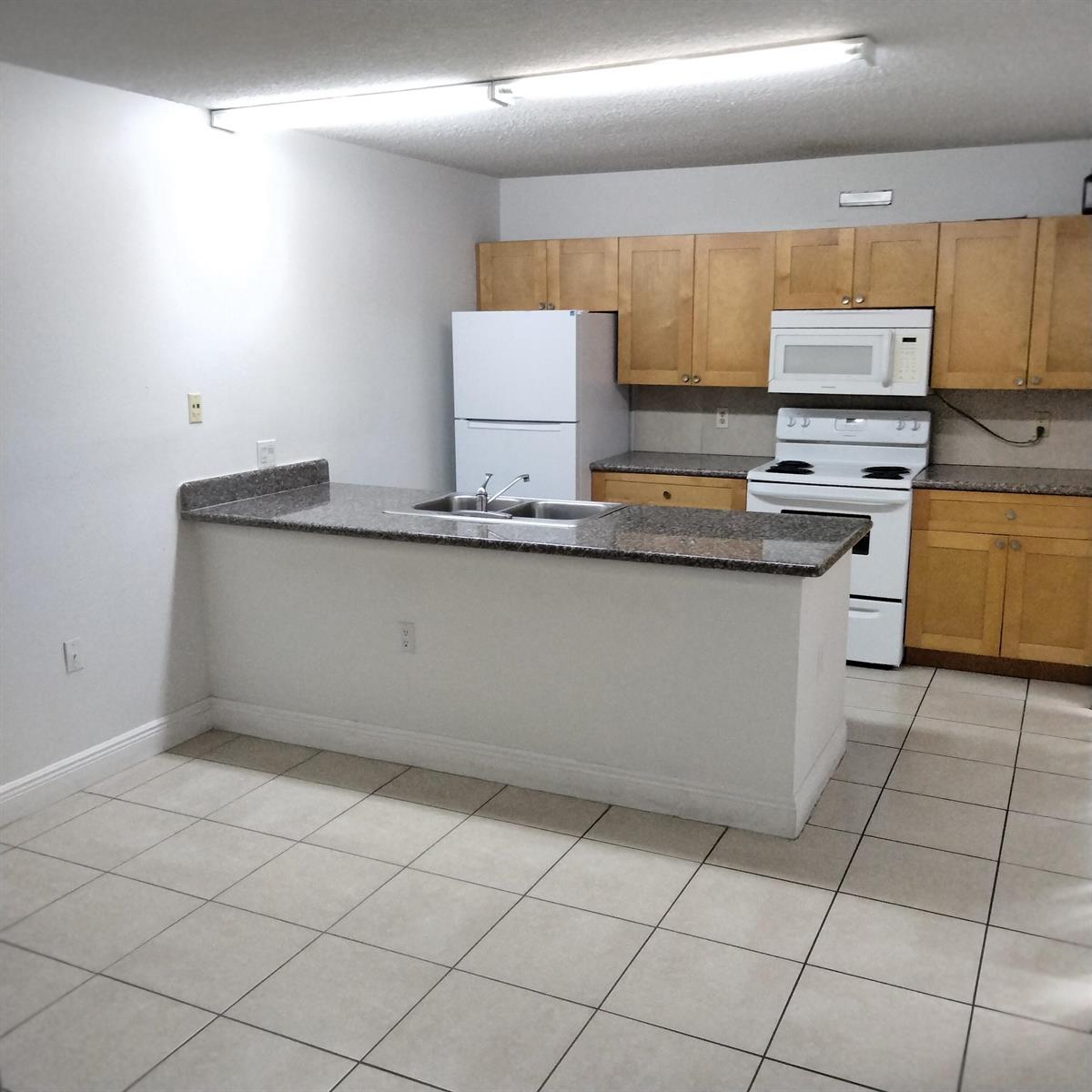 A kitchen features light wood cabinets, white appliances, a granite countertop island, and tiled flooring — 729 Mill Valley Place, West Palm Beach FL 33409, WEST PALM BEACH, FL