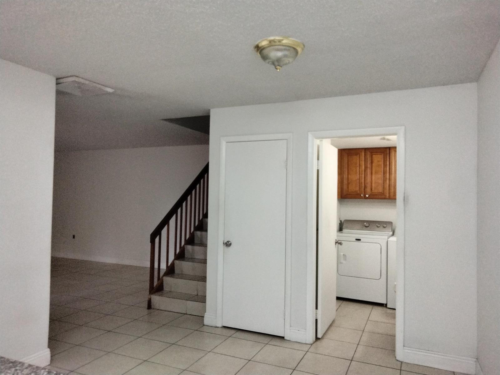 A room with tiled floors, a staircase, a closed door, and an open laundry room — 729 Mill Valley Place, West Palm Beach FL 33409, WEST PALM BEACH, FL