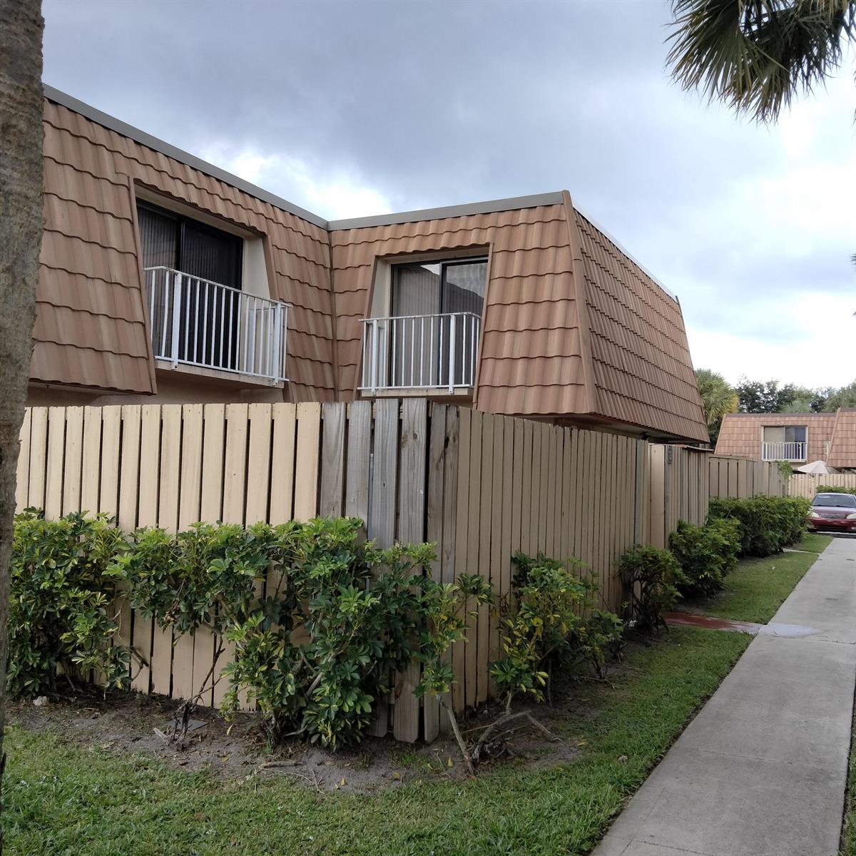 Exterior view of a two-story townhouse with a tan mansard roof and wooden privacy fence — 729 Mill Valley Place, West Palm Beach FL 33409, WEST PALM BEACH, FL