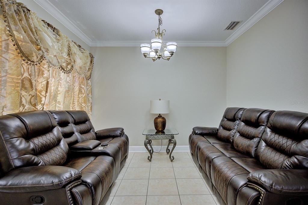 A living room features two brown leather reclining sofas, a glass end table, and chandelier — 4050 PLACID LAKES BOULEVARD, LAKE PLACID, FL