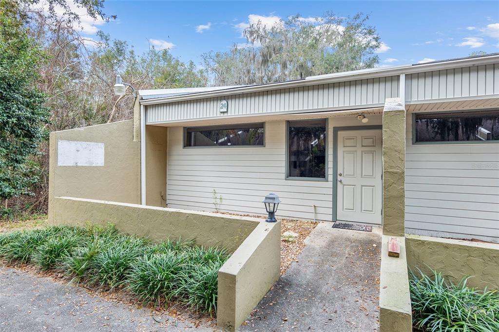 An exterior view of a single-story house with tan siding, a concrete walkway, and landscaping — 2801 SW COLLEGE ROAD UNIT 24, OCALA, FL