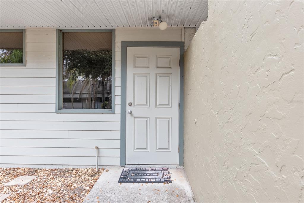 A white six-panel exterior door is set into a wall with horizontal siding and stucco — 2801 SW COLLEGE ROAD UNIT 24, OCALA, FL