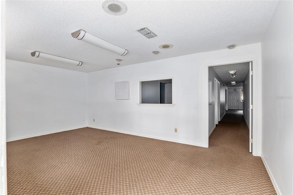 An empty room with beige carpet, white walls, fluorescent lighting, and a doorway to a hallway — 2801 SW COLLEGE ROAD UNIT 24, OCALA, FL