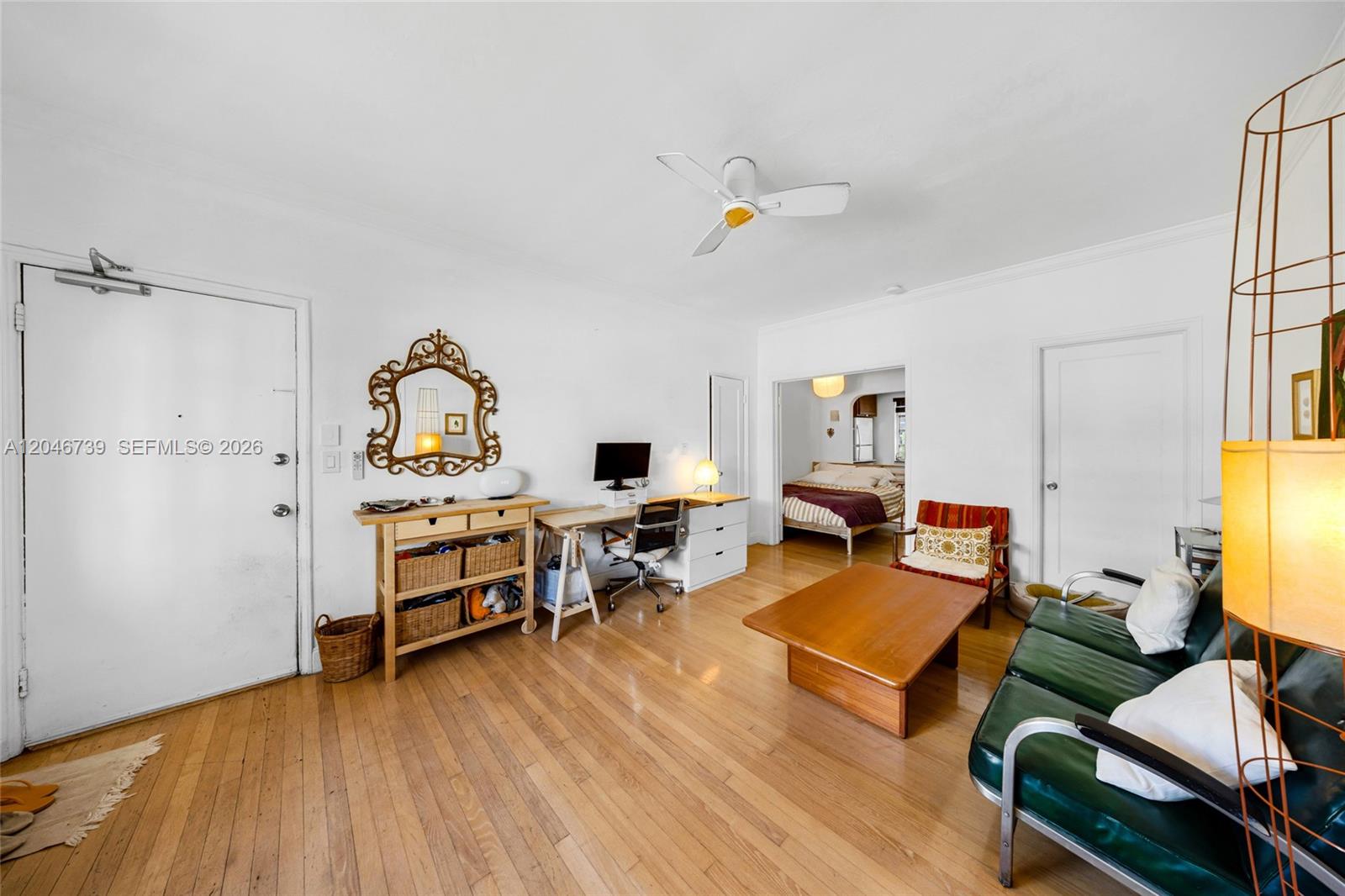 A living room with hardwood floors, a desk, a green sofa, and an adjacent bedroom — 1250 Drexel Ave # 8, Miami Beach FL 33139, MIAMI BEACH, FL