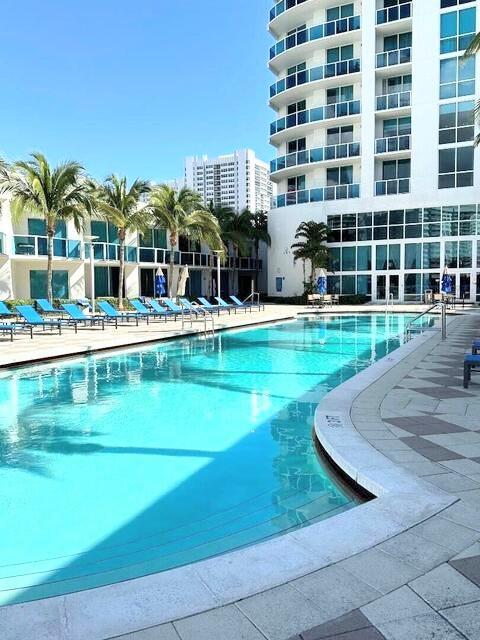 A swimming pool with lounge chairs sits in front of a tall, modern hotel building — 1945 S Ocean Drive # 701, Hallandale Beach FL 33009, HALLANDALE BEACH, FL