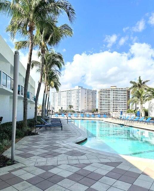 A swimming pool sits on a paved deck lined with palm trees and tall buildings — 1945 S Ocean Drive # 701, Hallandale Beach FL 33009, HALLANDALE BEACH, FL