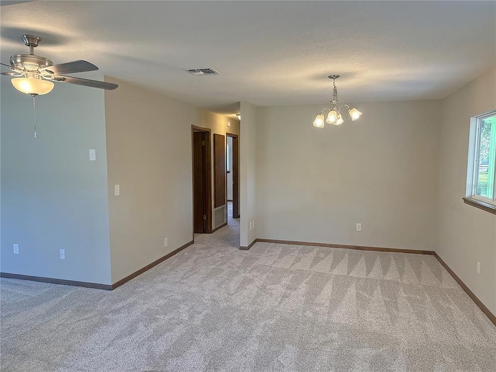 A carpeted living and dining area features a ceiling fan, chandelier, and neutral walls — 9095 SW 104TH LANE, OCALA, FL
