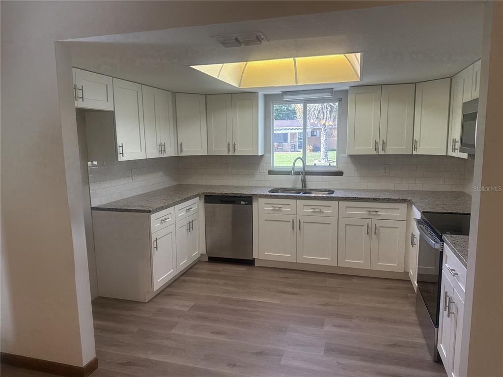A kitchen features white shaker cabinets, granite countertops, stainless steel appliances, and light wood flooring — 9095 SW 104TH LANE, OCALA, FL