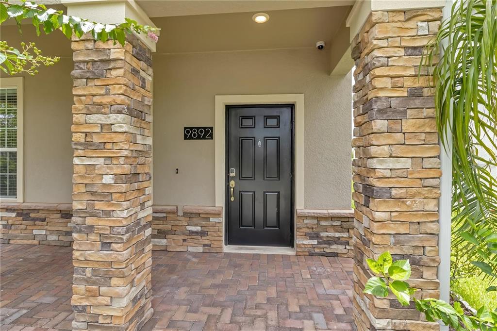 A front entryway features a black door, stone-clad pillars, and a brick paver porch — 9892 PECAN HICKORY WAY, ORLANDO, FL