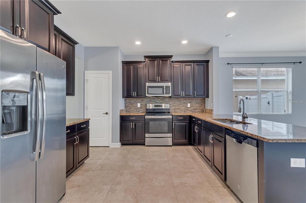 A kitchen features dark wood cabinets, stainless steel appliances, granite countertops, and light tile flooring — 9892 PECAN HICKORY WAY, ORLANDO, FL