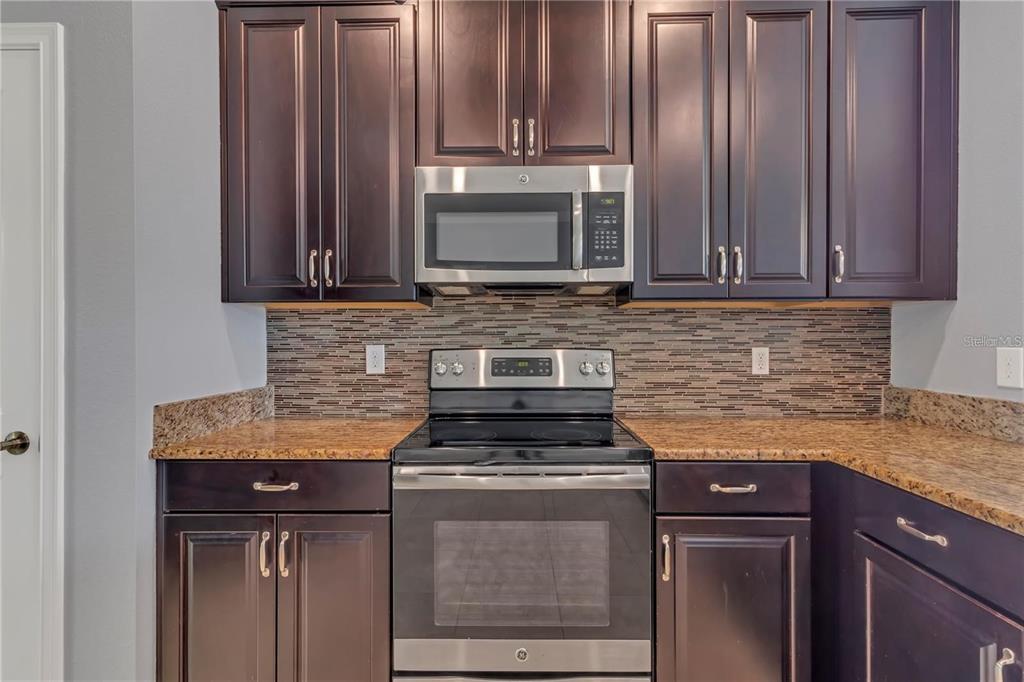 A kitchen features dark wood cabinets, stainless steel appliances, and a granite countertop — 9892 PECAN HICKORY WAY, ORLANDO, FL