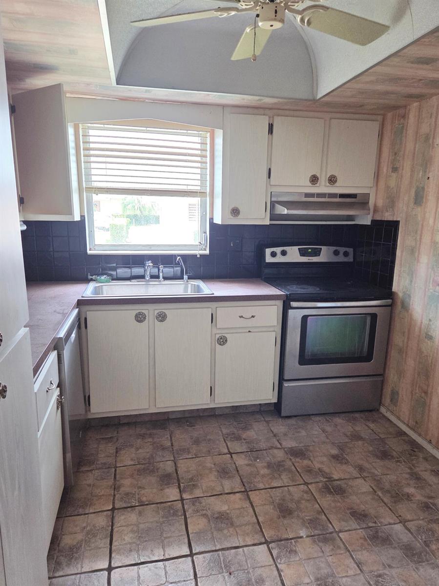 A kitchen features white cabinets, a stainless steel stove, black tile backsplash, and tiled flooring — 2703 Dudley Drive W, West Palm Beach FL 33415, WEST PALM BEACH, FL