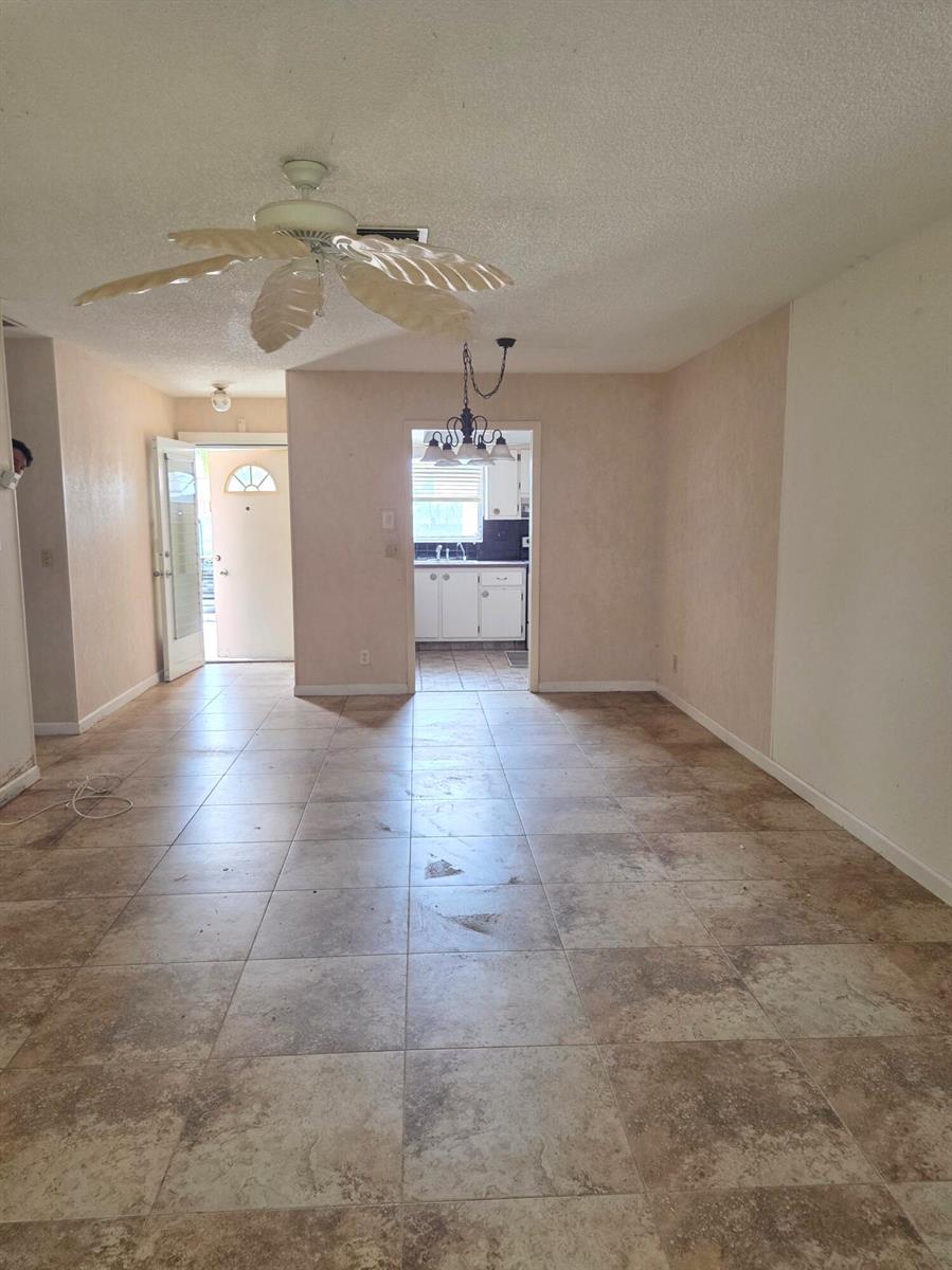 A room with tan tile flooring, a ceiling fan, and a doorway leading to a kitchen — 2703 Dudley Drive W, West Palm Beach FL 33415, WEST PALM BEACH, FL
