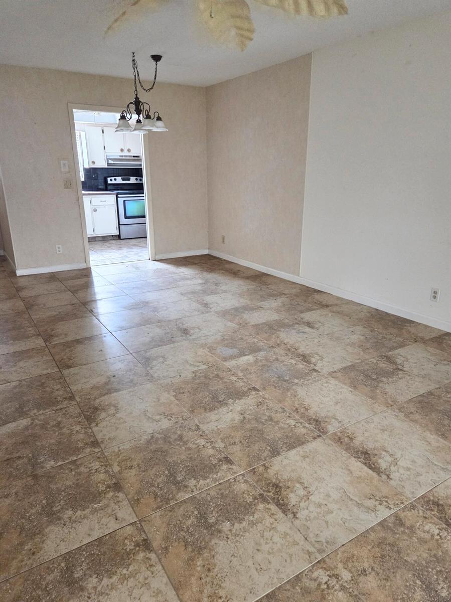 A dining area with large tan tile flooring leads into a kitchen with white cabinets — 2703 Dudley Drive W, West Palm Beach FL 33415, WEST PALM BEACH, FL
