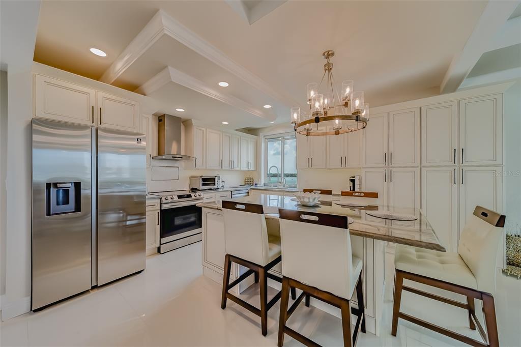 A white kitchen features a stainless steel refrigerator, a center island, and a chandelier — 1460 GULF BOULEVARD UNIT 1210, CLEARWATER BEACH, FL