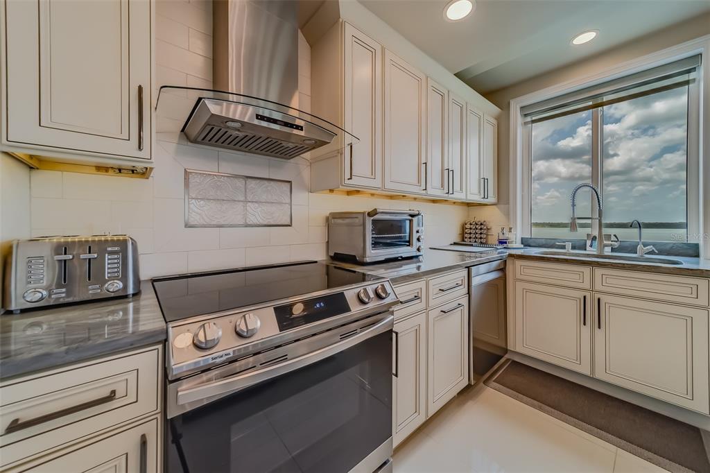 A kitchen features white cabinets, stainless steel appliances, a glass-top stove, and a window view — 1460 GULF BOULEVARD UNIT 1210, CLEARWATER BEACH, FL