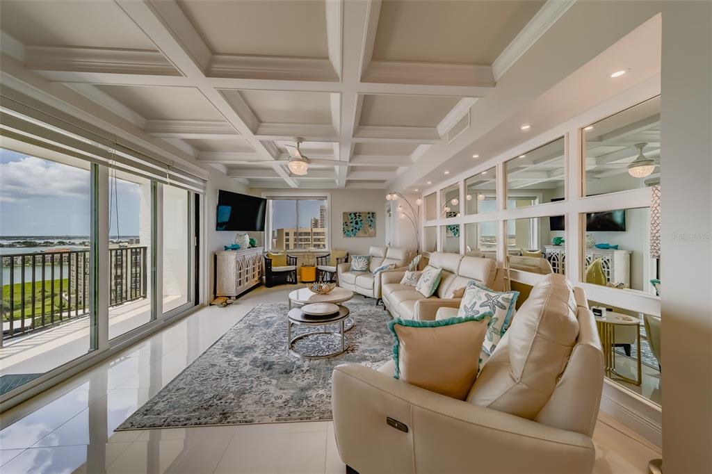 A living room features a coffered ceiling, mirrored wall panels, and a balcony with water views — 1460 GULF BOULEVARD UNIT 1210, CLEARWATER BEACH, FL