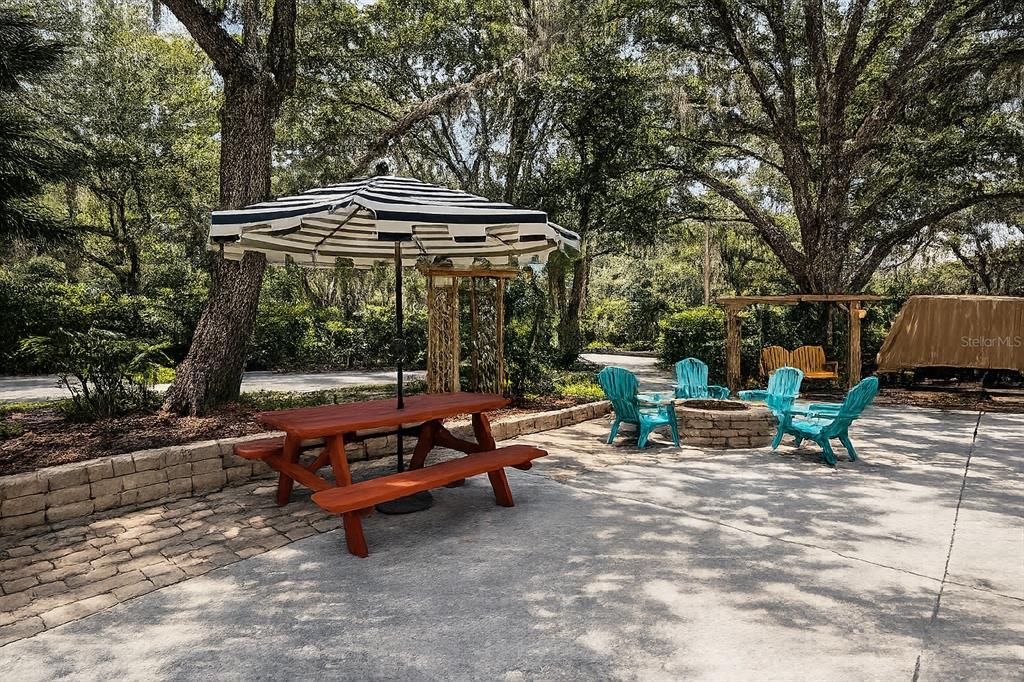 A patio features a picnic table with a striped umbrella, fire pit, and blue chairs — 243 SADDLE LANE, RIVER RANCH, FL