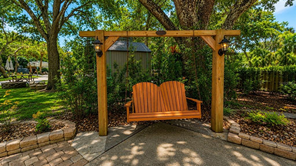 A wooden porch swing hangs from a pergola frame in a landscaped backyard — 243 SADDLE LANE, RIVER RANCH, FL