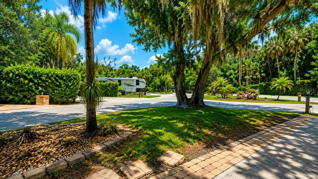 A paved driveway leads toward a parked recreational vehicle surrounded by trees and landscaping — 243 SADDLE LANE, RIVER RANCH, FL